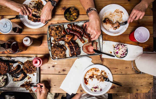 A group of people enjoying BBQ on a wooden table.