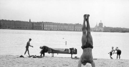 A man demonstrating fundamentals of bodyweight exercise with a handstand on the beach.