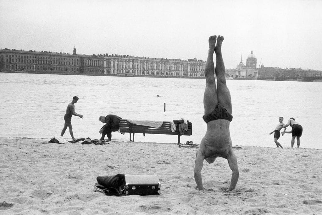 A man demonstrating fundamentals of bodyweight exercise with a handstand on the beach.