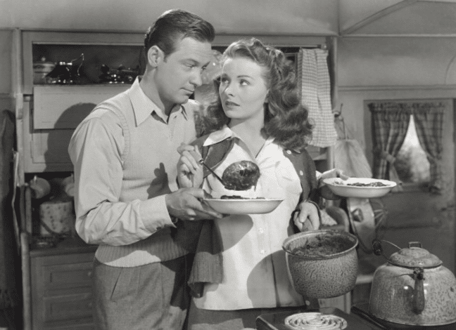 A man and woman, married, standing in a kitchen with a plate of food.