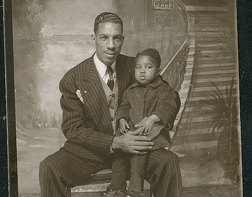 A man and a child sit on a chair, portraying a heartwarming fatherly moment.