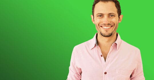A man smiling on a green screen during a podcast recording.