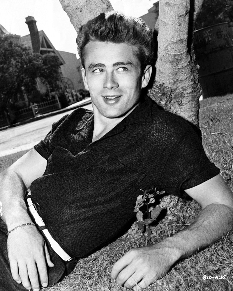 Vintage young man wearing wool polo shirt lying against tree looking to the left.
