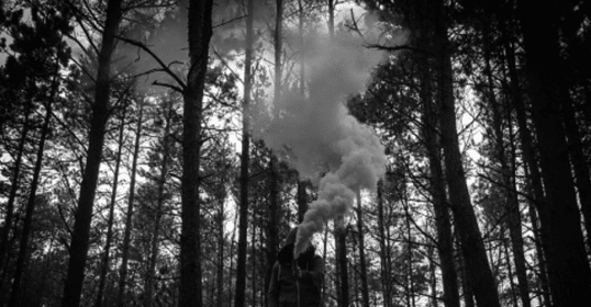 A quick snapshot of a person standing in the woods, captured in black and white.