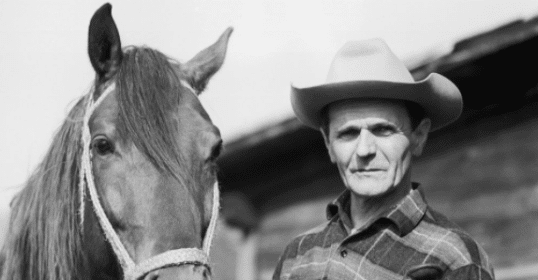 A real man in a cowboy hat standing next to a horse.