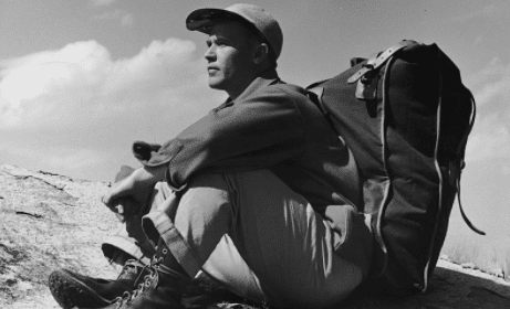 A man sitting on top of a mountain with a backpack, contemplating the value of solitude.
