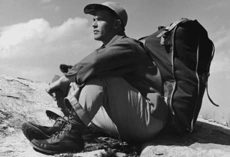 A man sitting on top of a mountain with a backpack, contemplating the value of solitude.