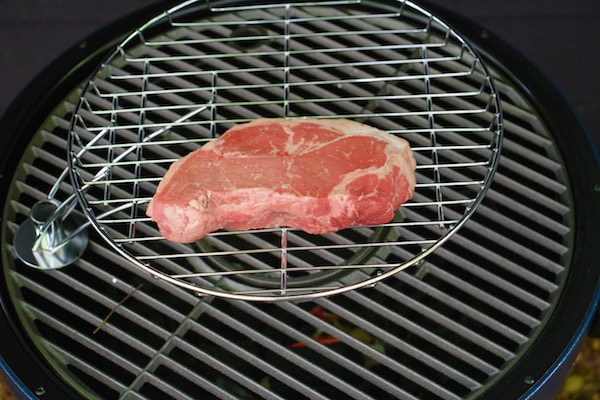 Large steak being cooked on grill indirect heat.