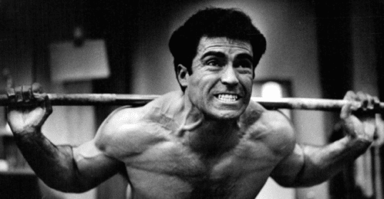 A man embracing the grind by lifting a barbell in a gym.