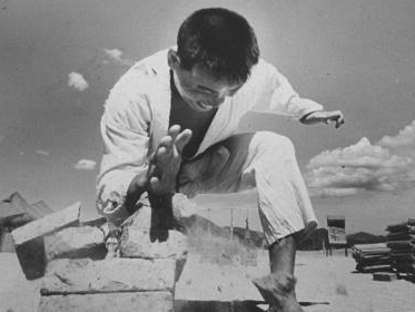 An old black and white photo of a man perfecting his kicks on bricks.