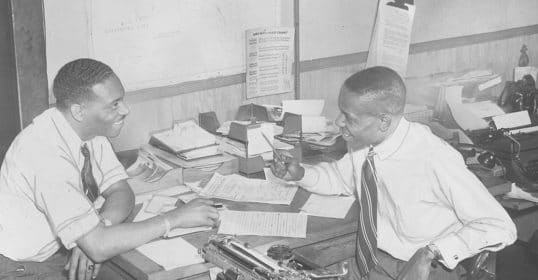 Two entrepreneurs sitting at a desk with a typewriter.