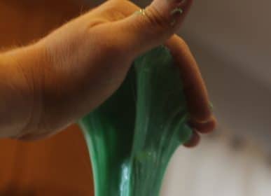 A kid-safe individual holding a piece of green slime at home.