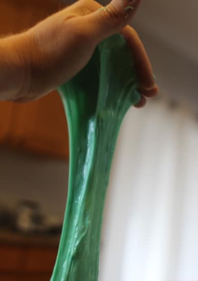 A kid-safe individual holding a piece of green slime at home.