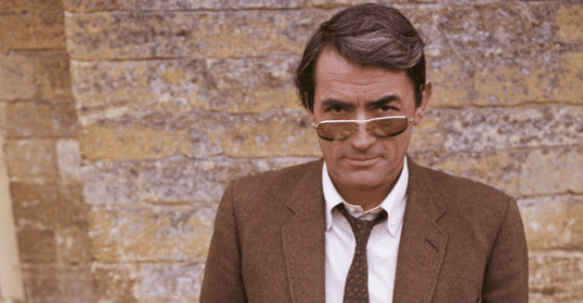 A man in sunglasses stands casually against a brick wall.