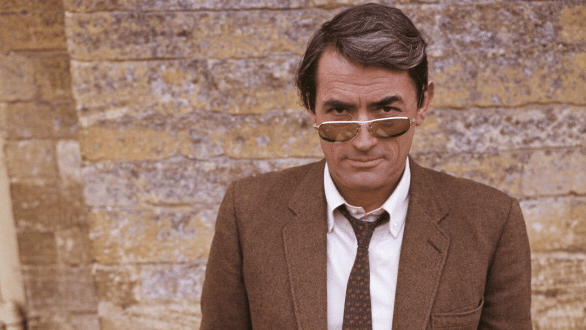 A man in sunglasses stands casually against a brick wall.