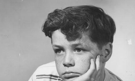 A black and white photo of a boy resting his chin on his hand.