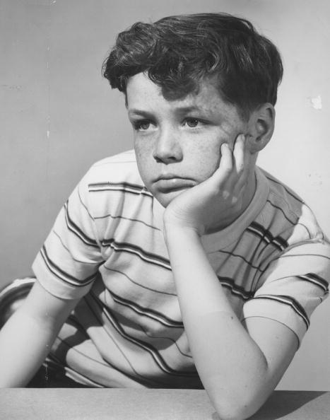 A black and white photo of a boy resting his chin on his hand.