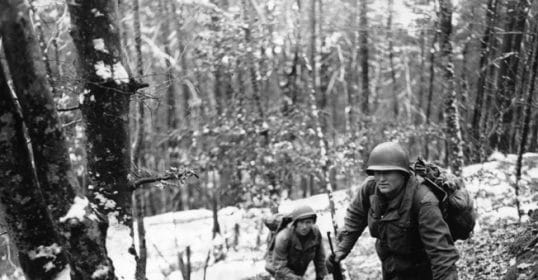A group of soldiers keep walking through the wilderness.