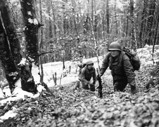 A group of soldiers keep walking through the wilderness.