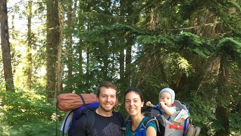 A man and woman hiking with a baby in backpacks.