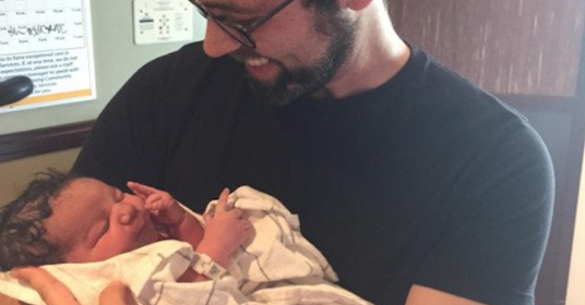 A man holding a baby in a hospital room, considering adoption.