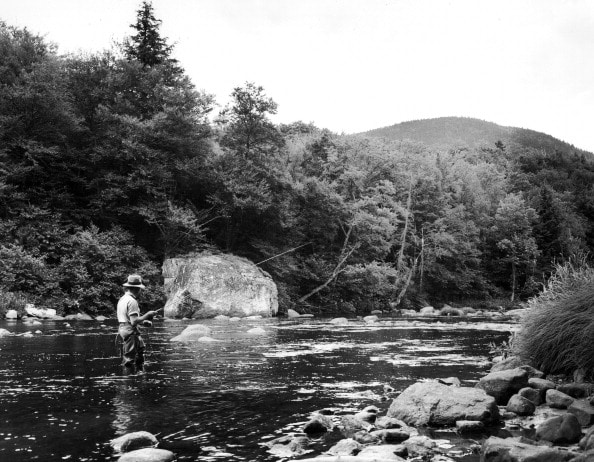 Learn how to fly fish in a river by studying this old black and white photo of a man fishing.