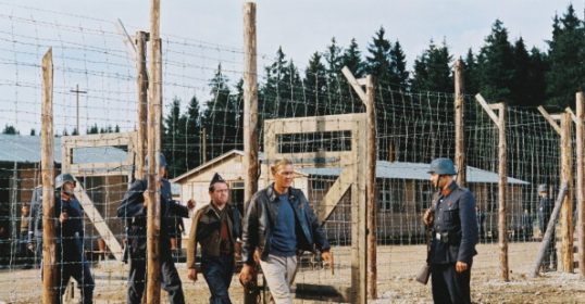 A group of people standing in front of a fence at a prisoner of war camp.
