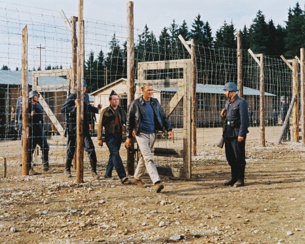 A group of people standing in front of a fence at a prisoner of war camp.