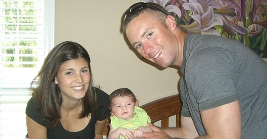 A soldier and his wife are posing for a picture with their baby.