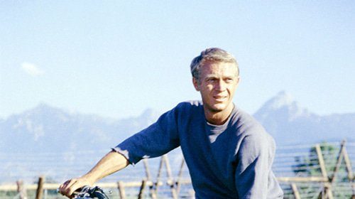 A man sitting on a motorcycle in a field, reminiscent of the iconic Steve McQueen from the Great Escape movie.