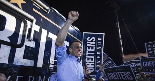 A man, possibly Gov. Eric Greitens, exhibits leadership by holding up signs in front of a crowd.