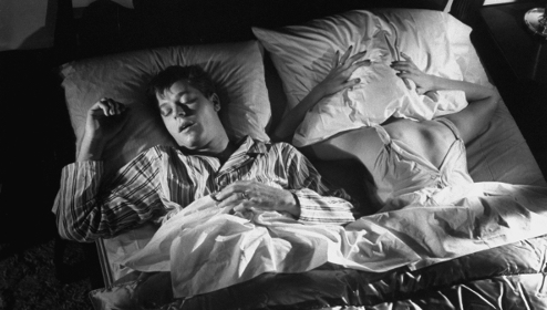 A man and a woman sleeping in bed, with the man snoring loudly.