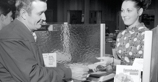 A man and woman making a cash deposit at the register.