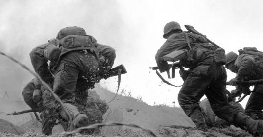 A black and white photo of soldiers on a hill, presumably fighting.