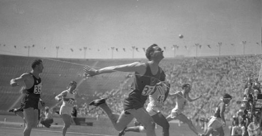 A group of men, half-heartedly running on a track at an olympic stadium.