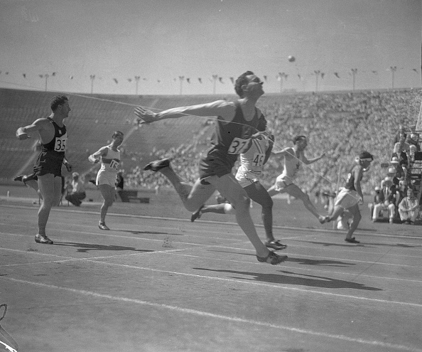 A group of men, half-heartedly running on a track at an olympic stadium.