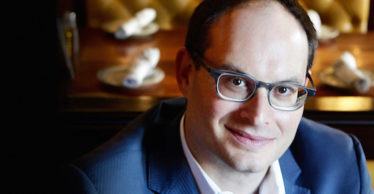 A man in glasses is smiling at a table.
