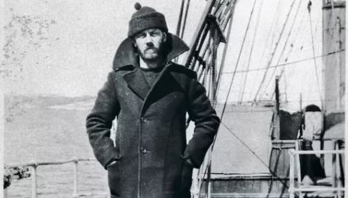 A man in a pea coat standing on the deck of a ship.