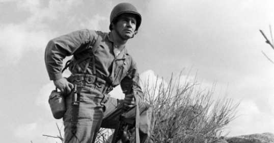 A Marine Corps soldier standing on top of a rock, showcasing his will to survive.