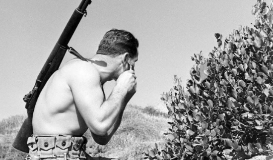 A man with a rifle in front of a bush showing fidelity to his surroundings.