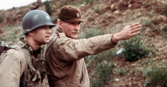 Two men in military uniforms pointing at each other in a dramatic fashion.