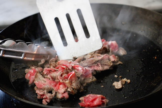 Chopping meat while frying in pan.