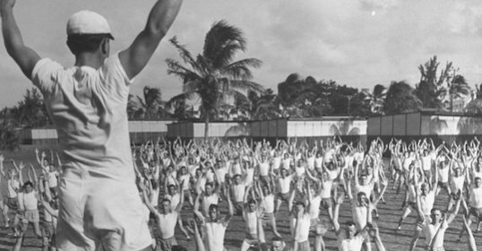 An old black and white photo of a group of people practicing yoga.