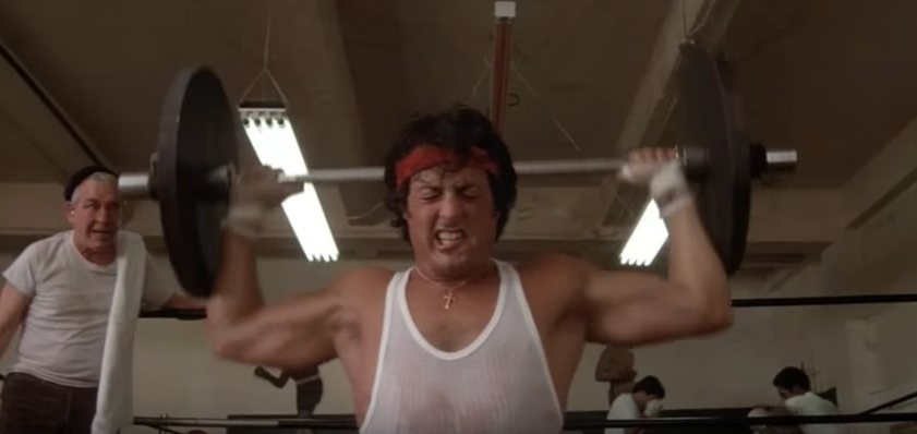 Rocky doing barbell presses while training.