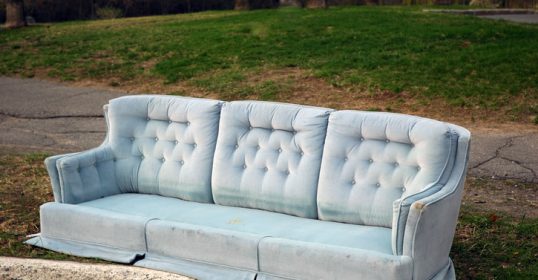 A large blue couch abandoned on the side of the road.
