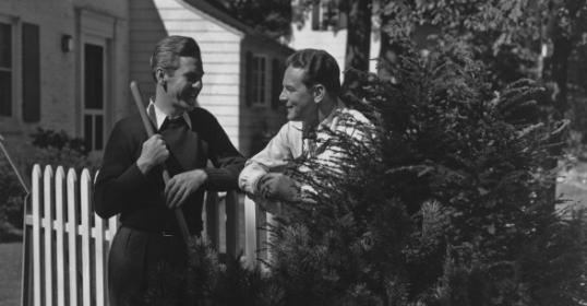 Two neighbors standing next to a white picket fence.