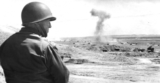 A man in a military uniform is observing an explosion.