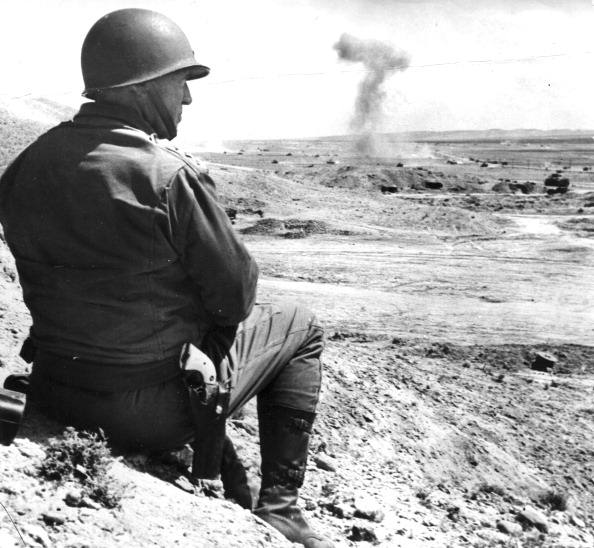 Soldier with a pistol watching out while sitting on a rock. 