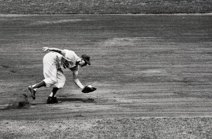 A reactive baseball player catches a ball in this black and white photo.