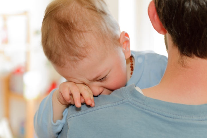 Sick baby crying on dad's shoulder. 